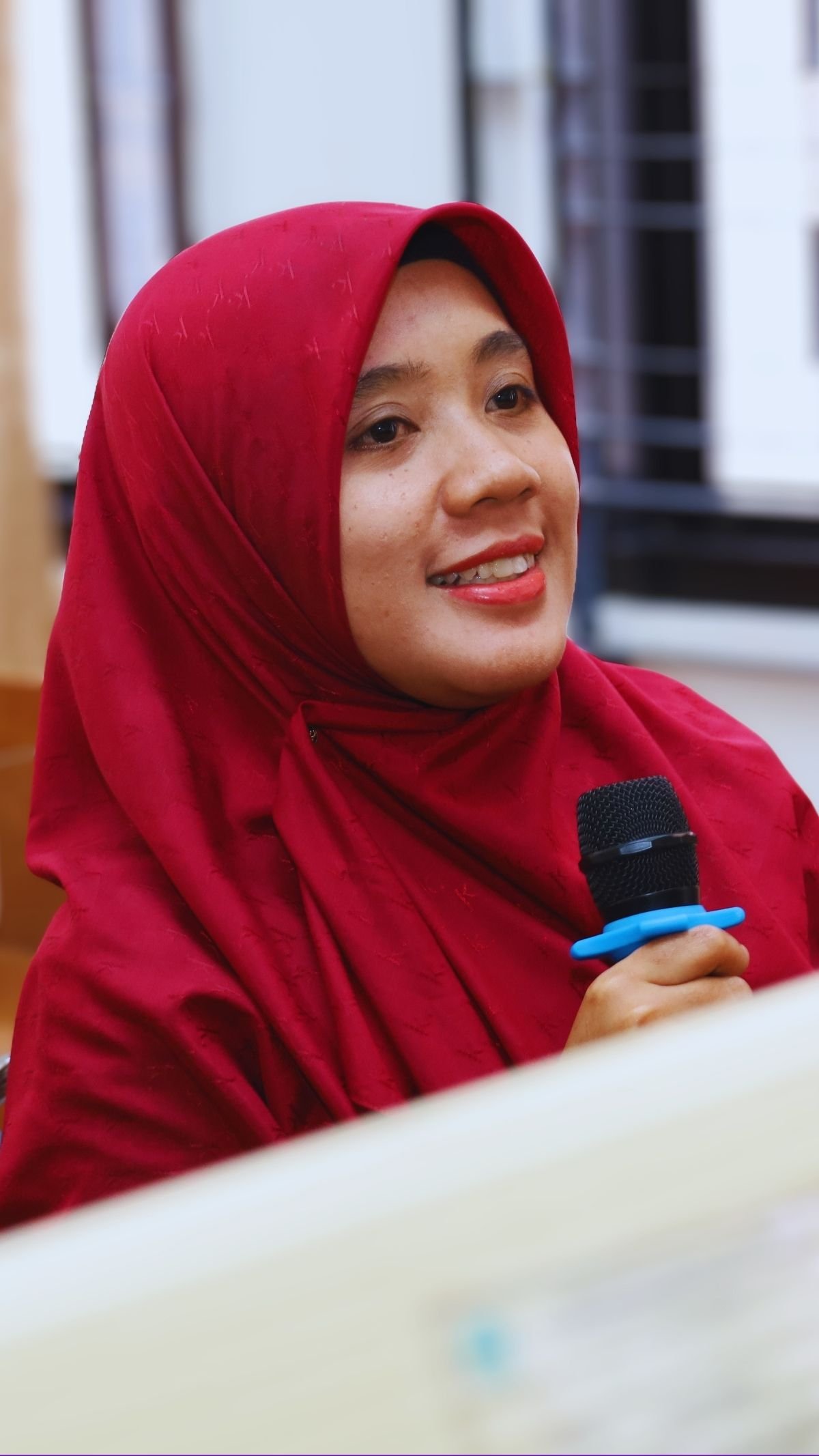 Peserta perempuan tersenyum sambil memegang mikrofon dalam sesi diskusi.